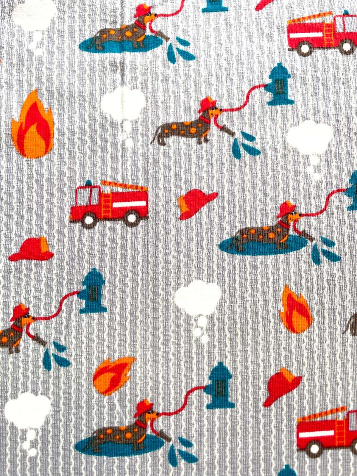 Detailaufnahme eines grau-weiß gestreiften Baumwolljerseys mit bunten Motiven: Dackel mit Feuerwehrhelmen, rote Feuerwehrautos und blaue Hydranten.