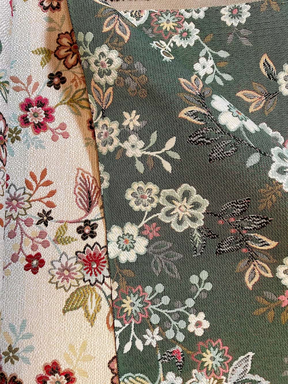 Drapierter Deko-Gobelinstoff als Meterware mit floralem Muster, gezeigt in den beiden Farbvarianten Dunkelgrün und Natur-Beige mit bunten Web-Blüten.