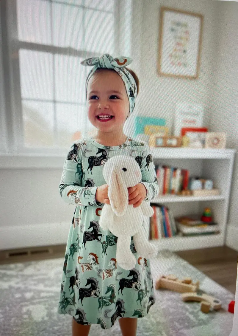 Weicher Baumwolljersey Stoff mit Pferdemuster als Meterware, verarbeitet zu einem hellgrünen Kinderkleid mit passendem Stirnband in einem hellen Kinderzimmer.