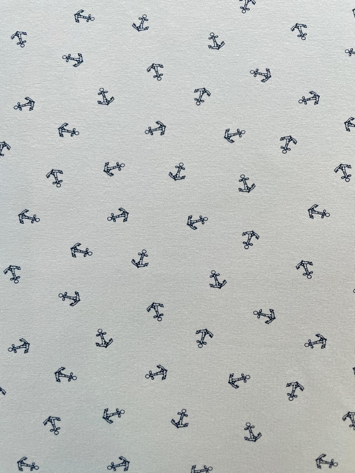 Nahaufnahme eines hellgrauen Baumwolljersey-Stoffes mit kleinen, dunkelblauen Ankern als Allover-Print. Ideale elastische Meterware für maritime Nähprojekte.