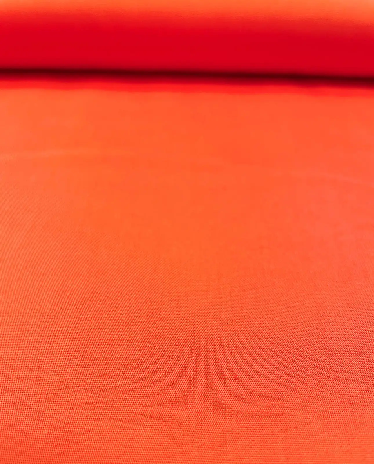 Nahaufnahme von feiner Baumwoll-Popeline als Meterware in einem kräftigen Orange. Die gleichmäßige und glatte Webstruktur des unifarbenen Baumwollstoffs ist im Bildvordergrund detailreich zu erkennen. Ideal für Sommerkleidung, Blusen und kreative DIY-Proj