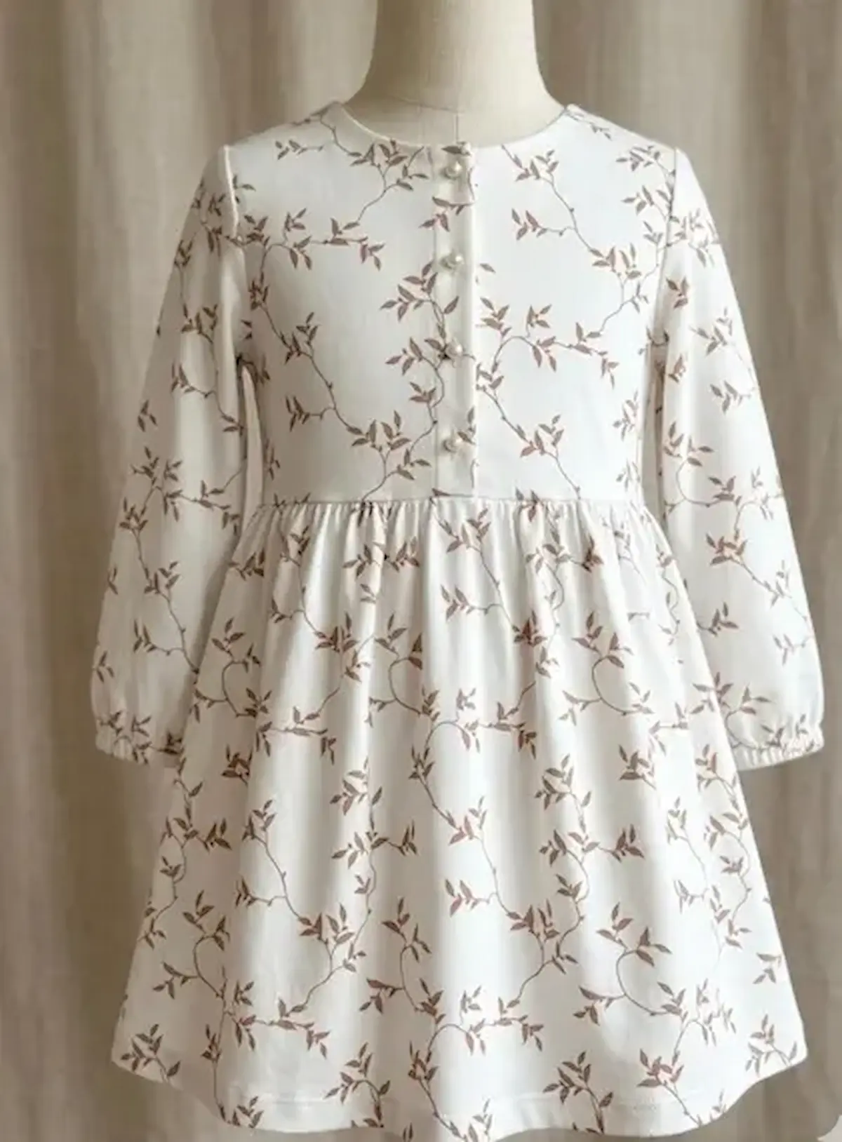 Handgenähtes Kinderkleid mit Knopfleiste aus cremefarbenem Jersey-Stoff mit terracottafarbenem Blätterranken-Print auf einer Schneiderpuppe