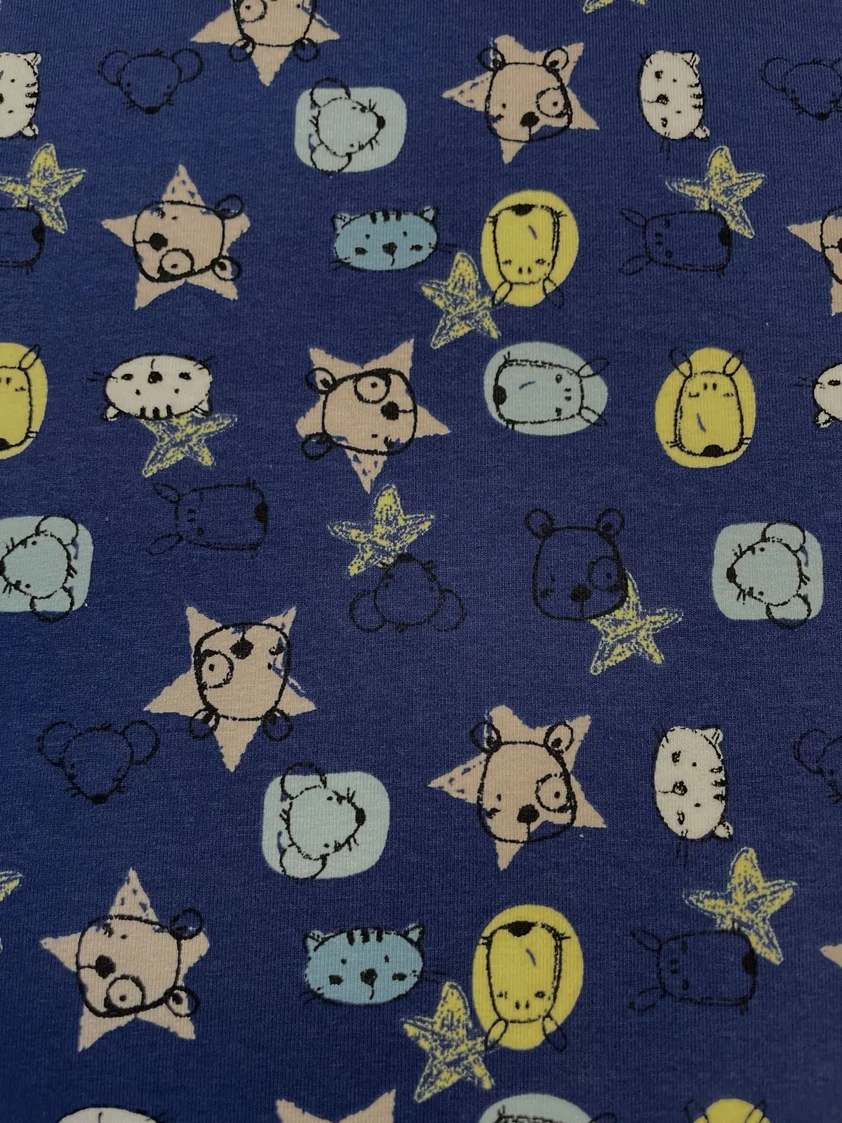 Hochwertiger Baumwolljersey als Meterware in Jeansblau, bedruckt mit einem niedlichen Allover-Muster aus kleinen Tiergesichtern im gezeichneten Doodle-Stil. Zu sehen sind Bären, Katzen und Mäuse in Beige, Hellblau und softem Gelb, umgeben von kleinen Ster