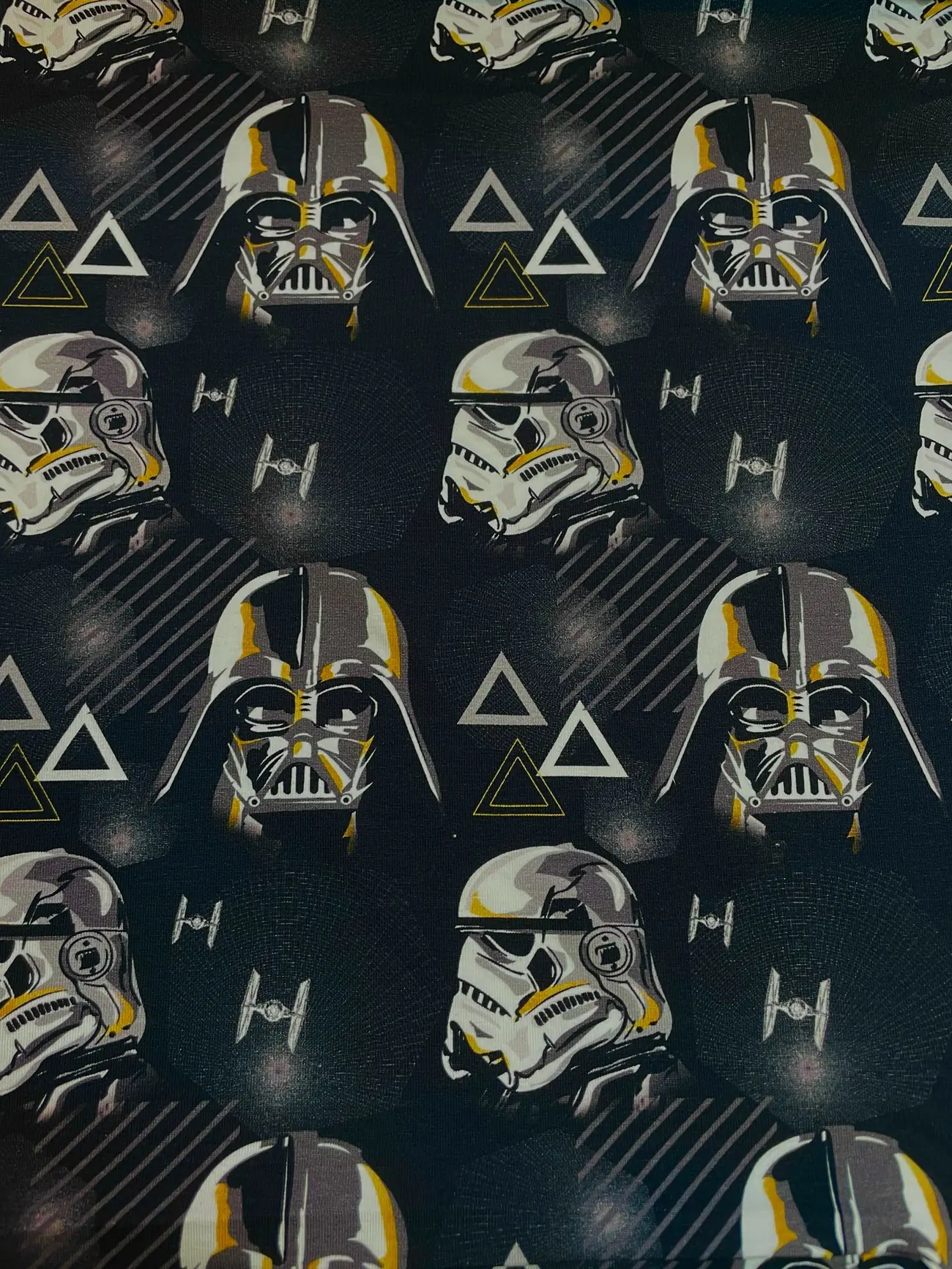 Schwarzer Baumwolljersey als Meterware, bedruckt mit einem coolen Muster aus den Masken von Darth Vader und Stormtroopern, kleinen TIE-Fightern und grafischen Dreiecken.