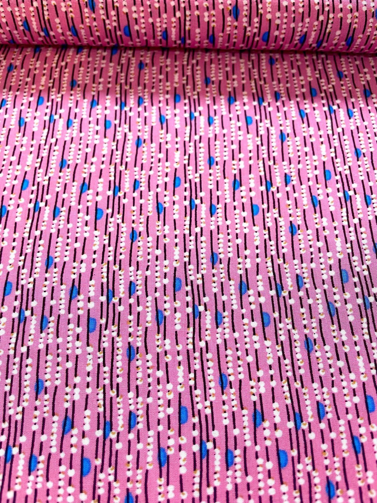 Nahaufnahme eines pinken Viskosestoffs mit vertikalem Linienmuster, weißen Punkten und blauen Details.