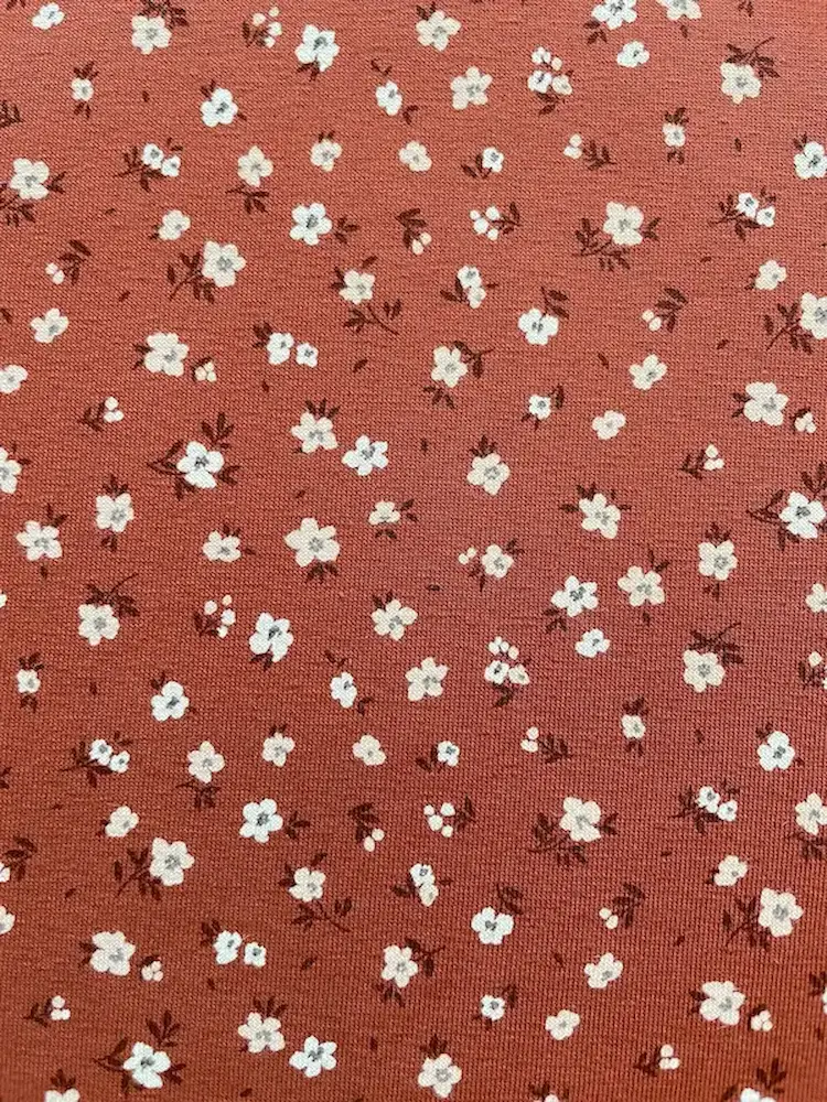 Weicher Jerseystoff in Rostbraun mit zierlichem weißen Blumenmuster, ideal für Kinderkleidung und Damenmode