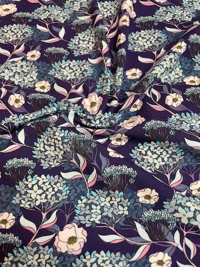 Hochwertiger Jersey-Stoff mit filigranem floralem Muster. Zu sehen sind hellblaue Hortensien und kleine rosa Blüten auf einem tiefdunkelblauen Hintergrund. Ideal für Kleider und Shirts.