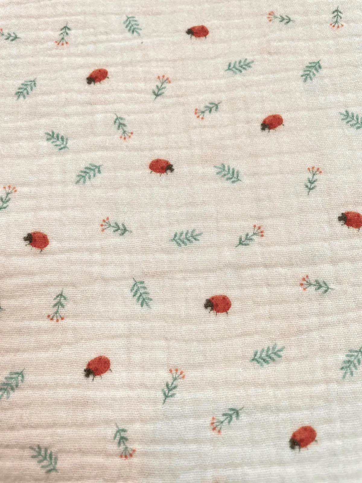 Weicher Baumwoll-Musselin in Creme mit kleinen Marienkäfern und grünen Zweigen, luftiger Double Gauze für Baby-Erstausstattung.
