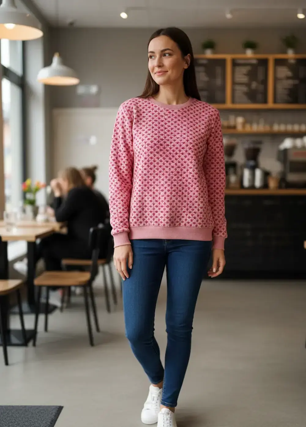 Frau trägt einen Pullover aus French Terry Stoff mit rosa Rautenmuster in einem Café.