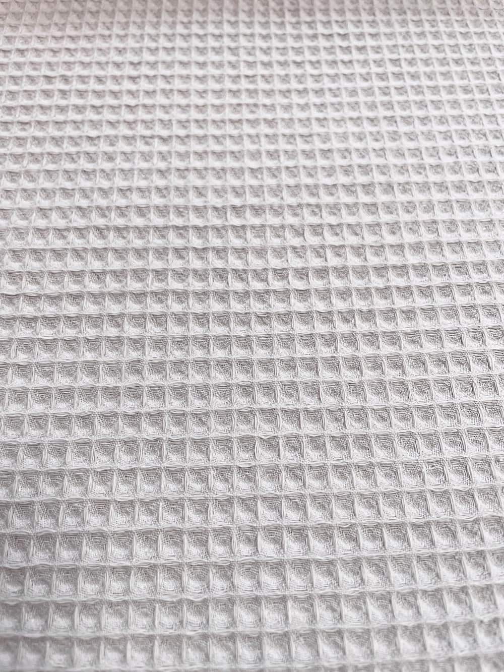 Nahaufnahme von hellgrauem Waffelpique Stoff als Meterware mit feiner Waffelstruktur für Bademäntel, Handtücher und Baby-Zubehör.