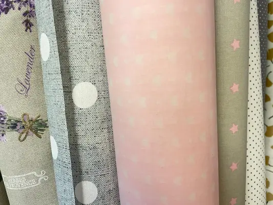 Sortiment an beschichteten Baumwollstoffen, darunter rosa Herzen, graue Punkte, Lavendel-Print und Sternen-Design, Meterware-Rollen.