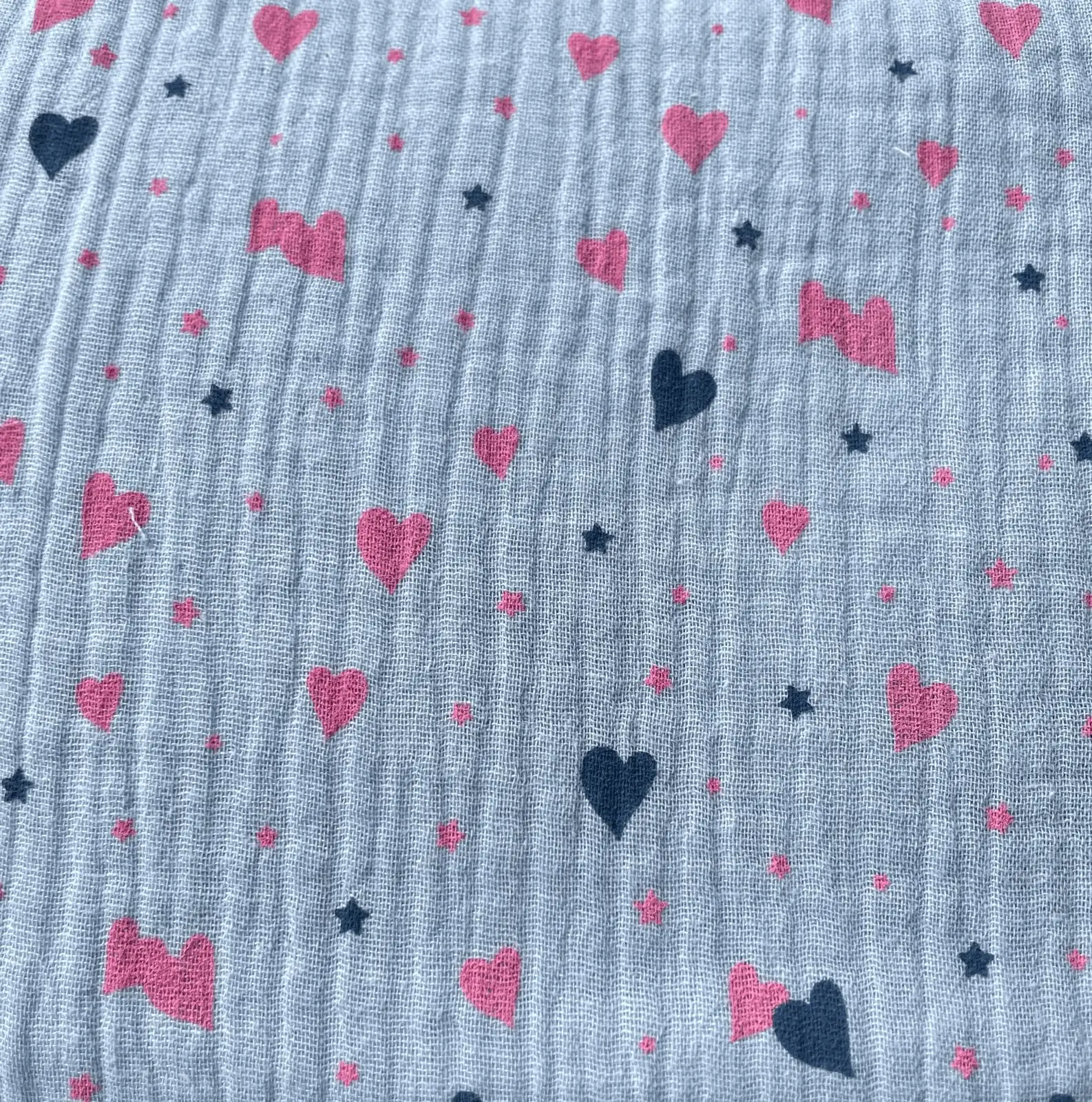 Weicher Musselin-Stoff in hellem Graublau, bedruckt mit rosa Herzen und dunkelblauen Sternen. Klassische Double-Gauze Baumwollqualität mit Crinkle-Optik für Kinderzimmer-Deko und Kleidung