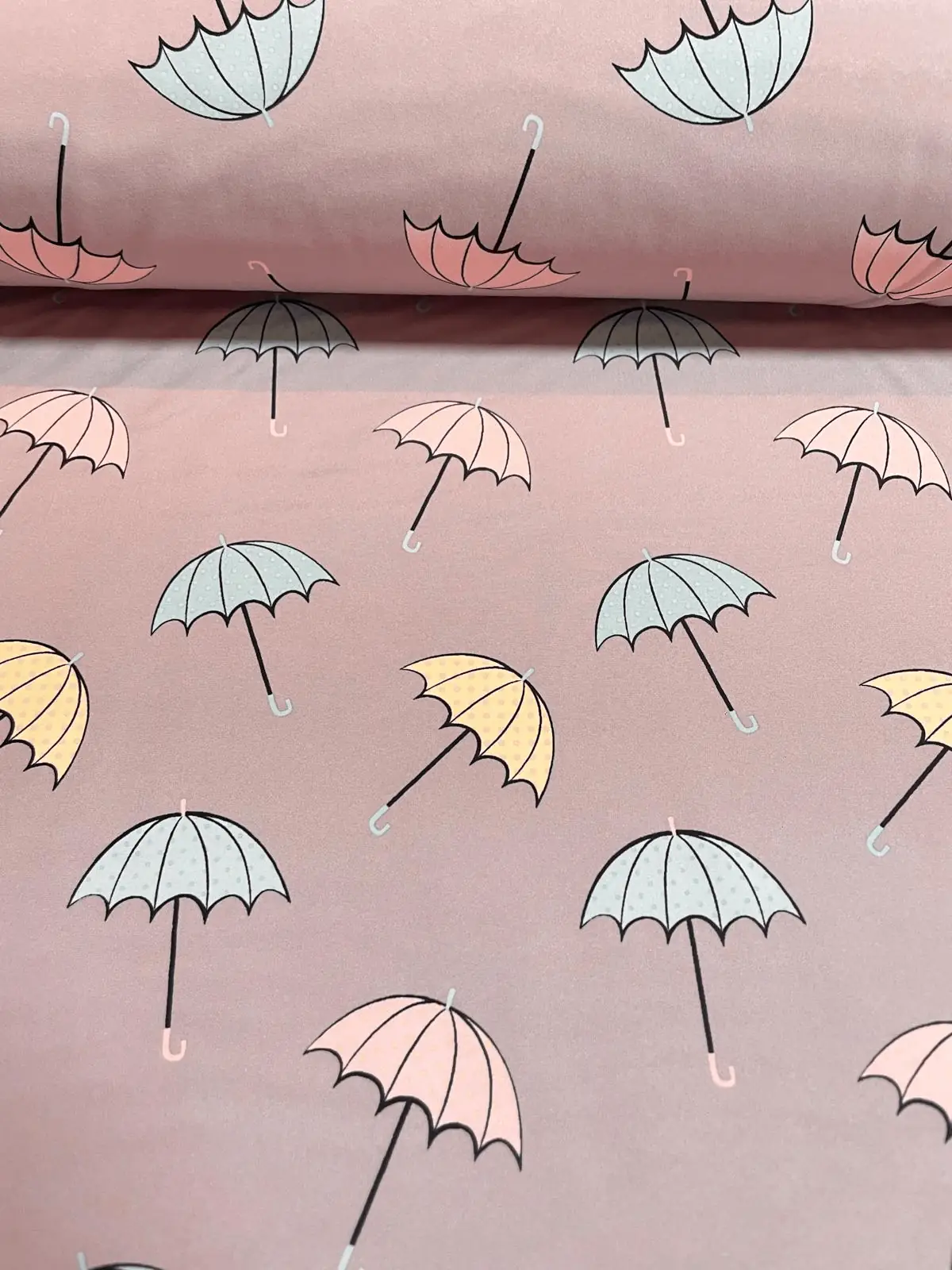 Outdoor-Softshell-Stoff in Altrosa, bedruckt mit filigranen Regenschirmen in Pastelltönen wie Hellblau, zartem Gelb und Rosa. Die Regenschirme haben schwarze Griffe und dezente Pünktlich-Muster. Hochwertiger Funktionsstoff für Mädchenjacken und Regenbekle