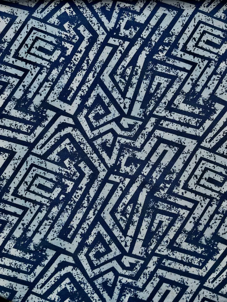 Nahaufnahme eines French Terry Stoffes mit einem abstrakten, geometrischen Labyrinth-Muster. Das Design besticht durch dunkelblaue Linien in Used-Optik auf einem hellblauen bis weißlichen Hintergrund. Hochwertiger Sommersweat als Meterware für moderne Bek