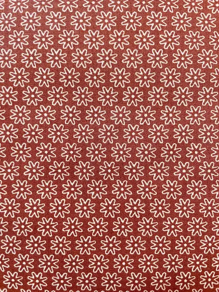 Hochwertige Baumwolle Webware Meterware in Rostbraun-Terrakotta mit einem gleichmäßigen, geometrischen Allover-Muster aus kleinen, weißen Retro-Blüten.