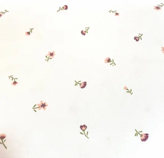 Weißer Jersey-Stoff mit einem feinen Muster aus kleinen, zarten Streublumen in Rosa, gedecktem Lila und grünen Stielen.