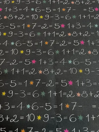 Beschichtete Baumwolle im Tafel-Design mit handgeschriebenen Rechenaufgaben und bunten Sternen, schwarz-weißer Schulstoff
