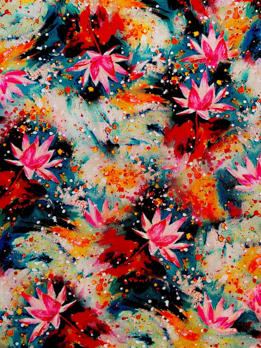 Farbenfroher Viskosestoff mit pinken Lotusblüten und abstrakten Farbspritzern in Orange, Rot und Teal; weich fließende Qualität.