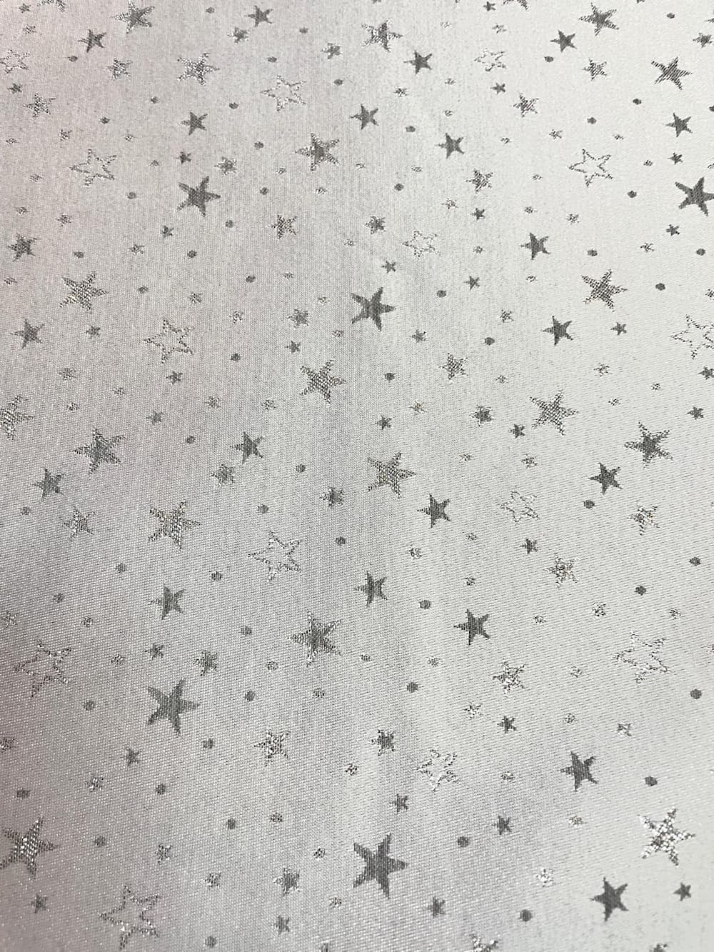 Dekostoff als Meterware mit einem Muster aus vielen kleinen und großen Sternen in Silber und Grau auf weißem oder hellgrauem Hintergrund.