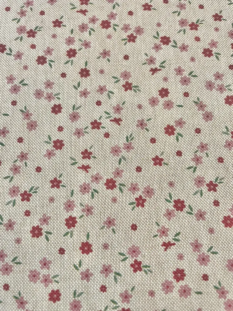 Strukturierter Dekostoff als Meterware mit kleinen, zarten Streublümchen in Rosa und Rot auf hellem Hintergrund in Leinenoptik.