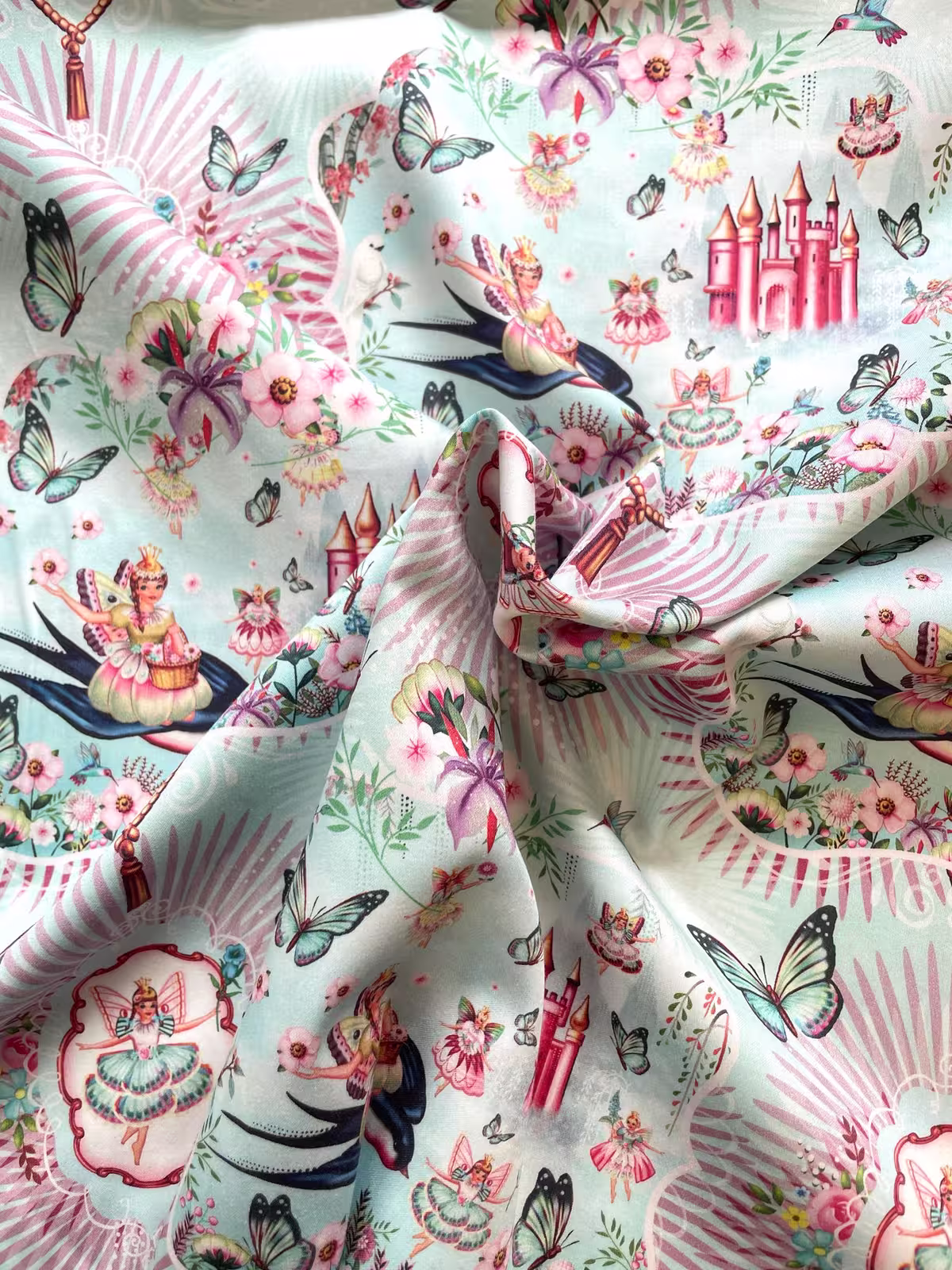 Hochwertiger Baumwoll-Satin Stoff in Hellblau mit detailreichem Märchen-Print: Feen, Schmetterlinge, Blumen und ein rosa Schloss in fließender Optik.