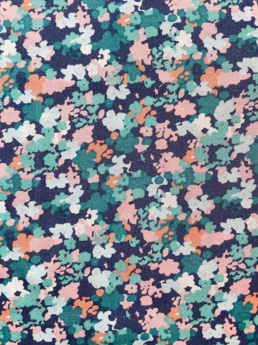 Nahaufnahme eines weich fließenden Viskosestoffs mit einem kleinteiligen, dichten Blumenmuster in Dunkelblau, Türkis, Rosa und Apricot.