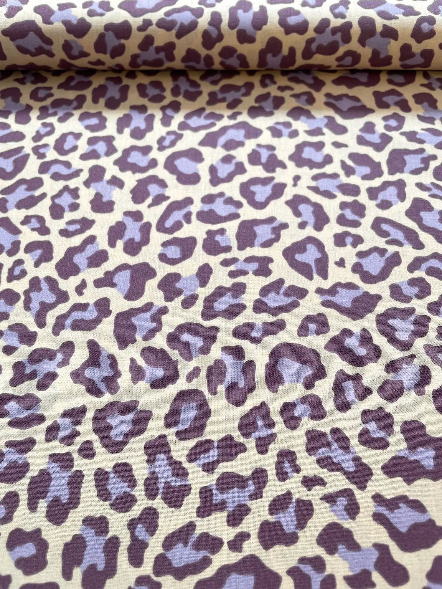 Hochwertiger Baumwollstoff mit modernem Leopardenmuster in Flieder und dunklem Lila auf hellem Hintergrund.