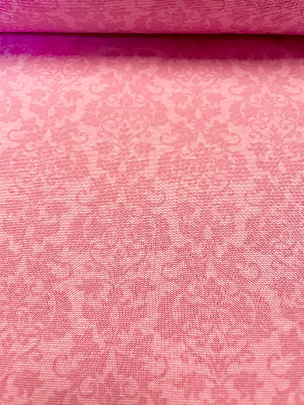 Nahaufnahme eines elastischen Bündchenstoffs mit barockem Ornament-Muster in verschiedenen Pink- und Rosatönen.