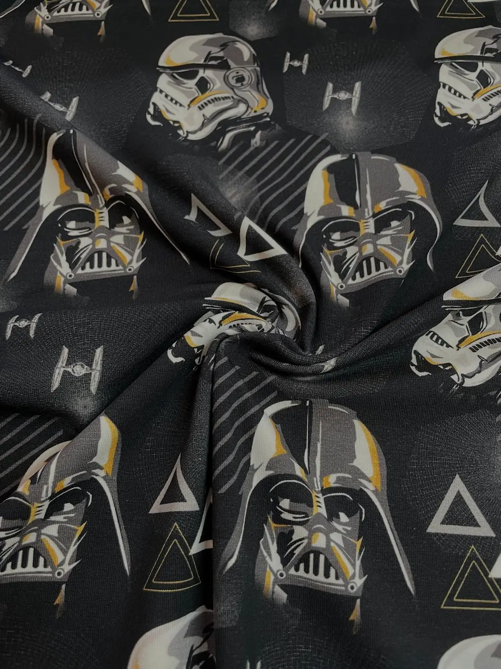 Ein kunstvoll drapierter, schwarzer Baumwolljersey-Stoff mit Faltenwurf, bedruckt mit Darth Vader Masken, Stormtrooper Helmen und TIE-Fightern.