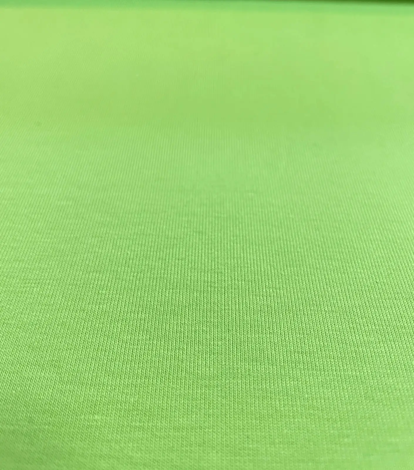 Eine detailreiche Nahaufnahme von einem unifarbenen, kräftig hellgrünen Baumwolljersey-Stoff als Meterware mit einer glatten, fein gestrickten Oberflächenstruktur.