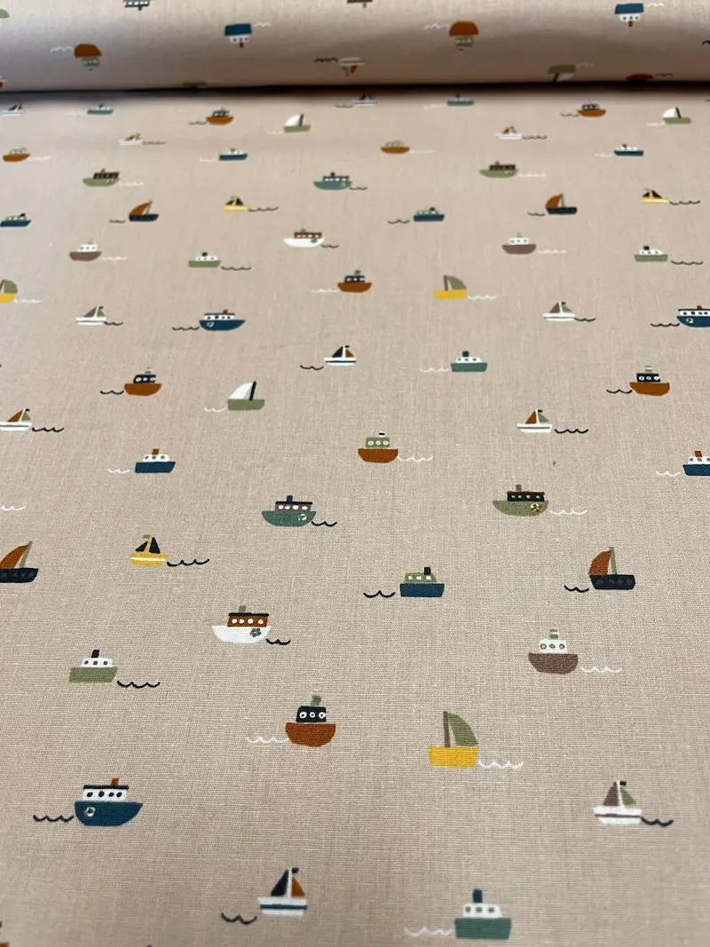 Draufsicht auf hellbraune bzw. beige Bio-Baumwoll-Popeline als Meterware mit einem feinen, minimalistischen Muster aus kleinen bunten Segelbooten und Dampfern auf minimalistischen Wellen