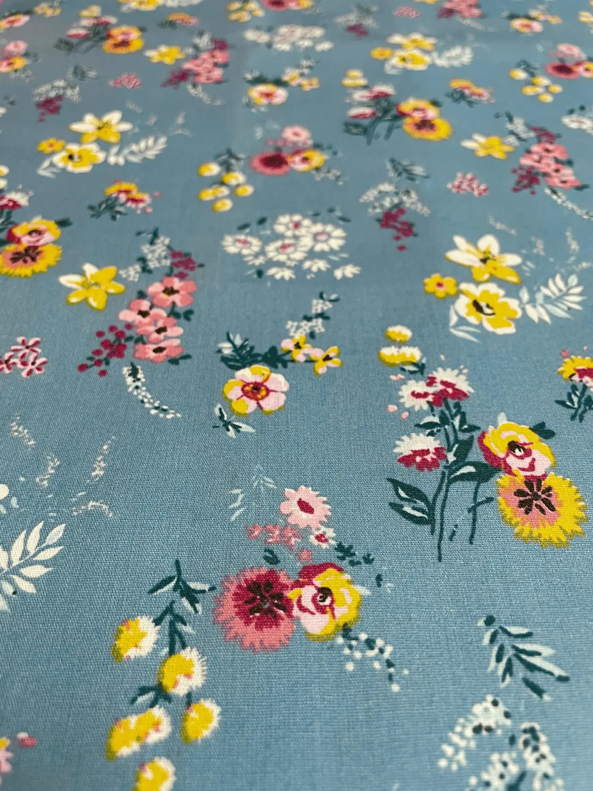 Hellblaue beschichtete Baumwolle mit bunten Blumenwiesen-Print (gelbe, rosa und weiße Blüten), wasserabweisende Meterware