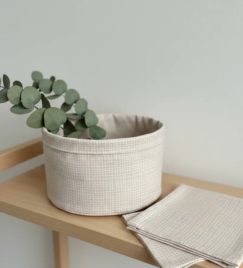 Strukturierte Nahaufnahme von feiner Baumwoll-Webware in hellem Puder-Apricot mit einem minimalistischen, wie von Hand gezeichneten weißen Gittermuster.