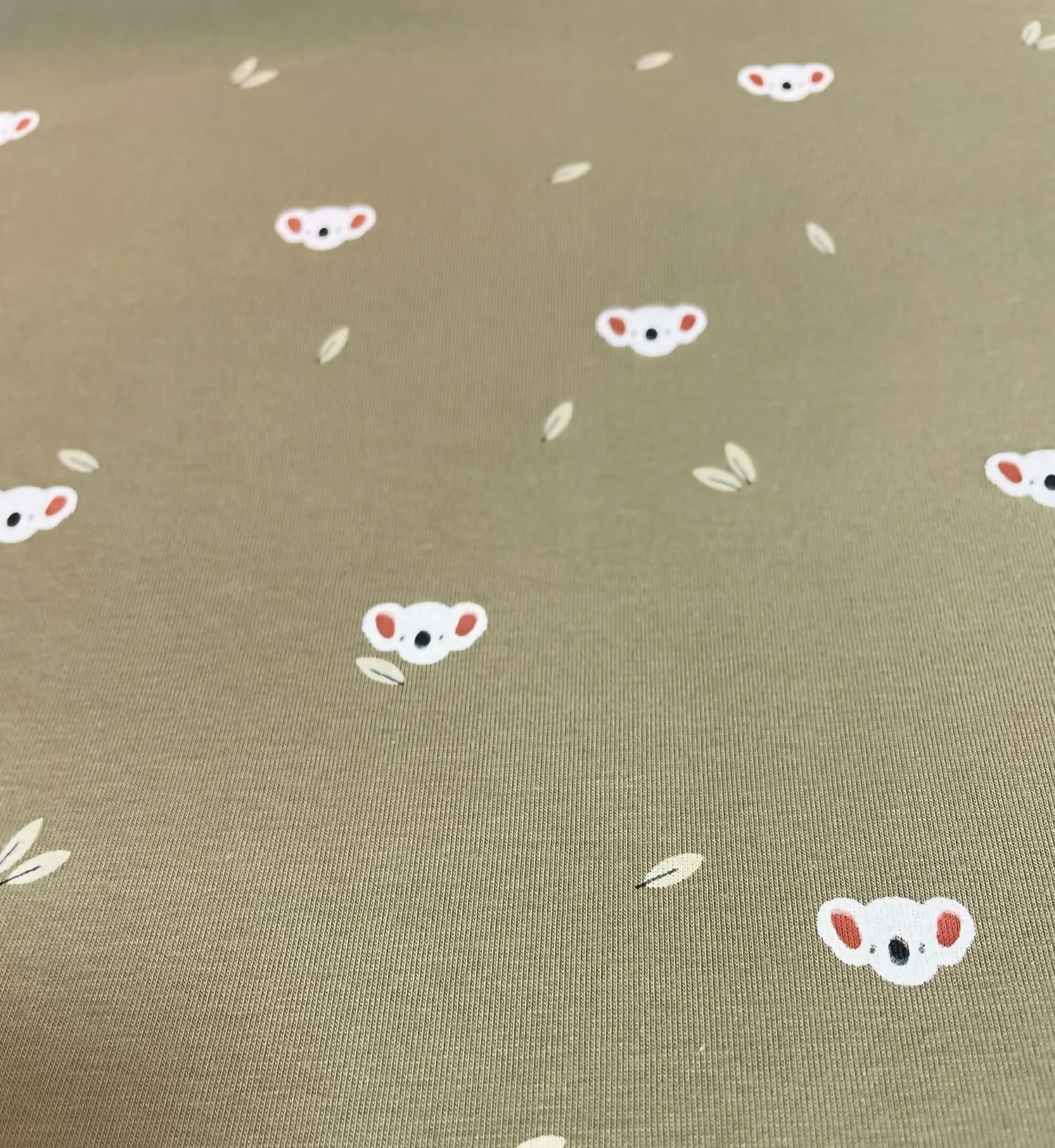 Olivgrüner Jersey-Stoff mit kleinen weißen Koalaköpfen und dezenten Blättern – minimalistisches Design für moderne Baby- und Kinderkleidung.
