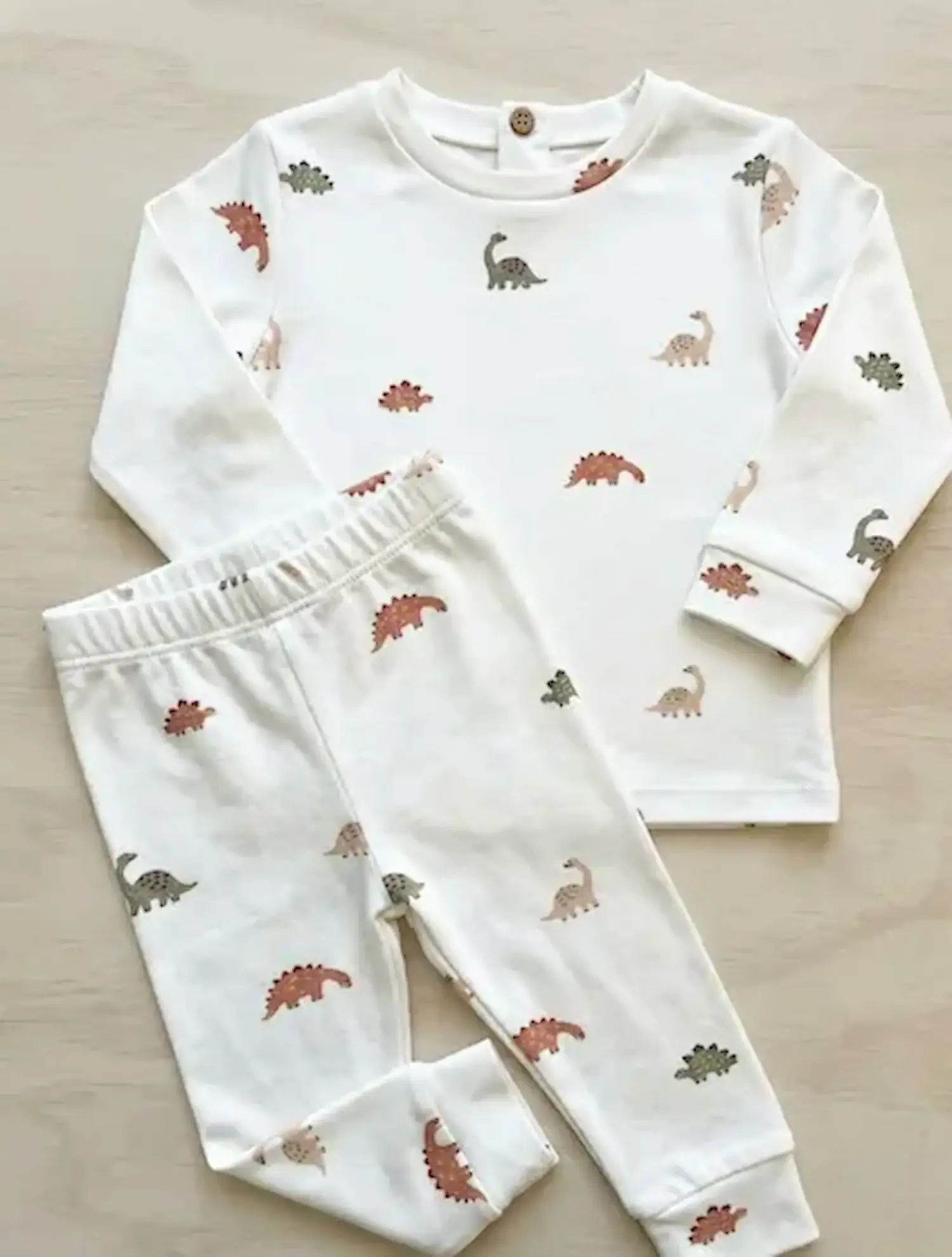 Zweiteiliger Kinder-Schlafanzug aus weißem Jersey-Stoff mit Allover-Dinosaurier-Print in Erd- und Naturtönen, bestehend aus Langarmshirt und passender Hose.