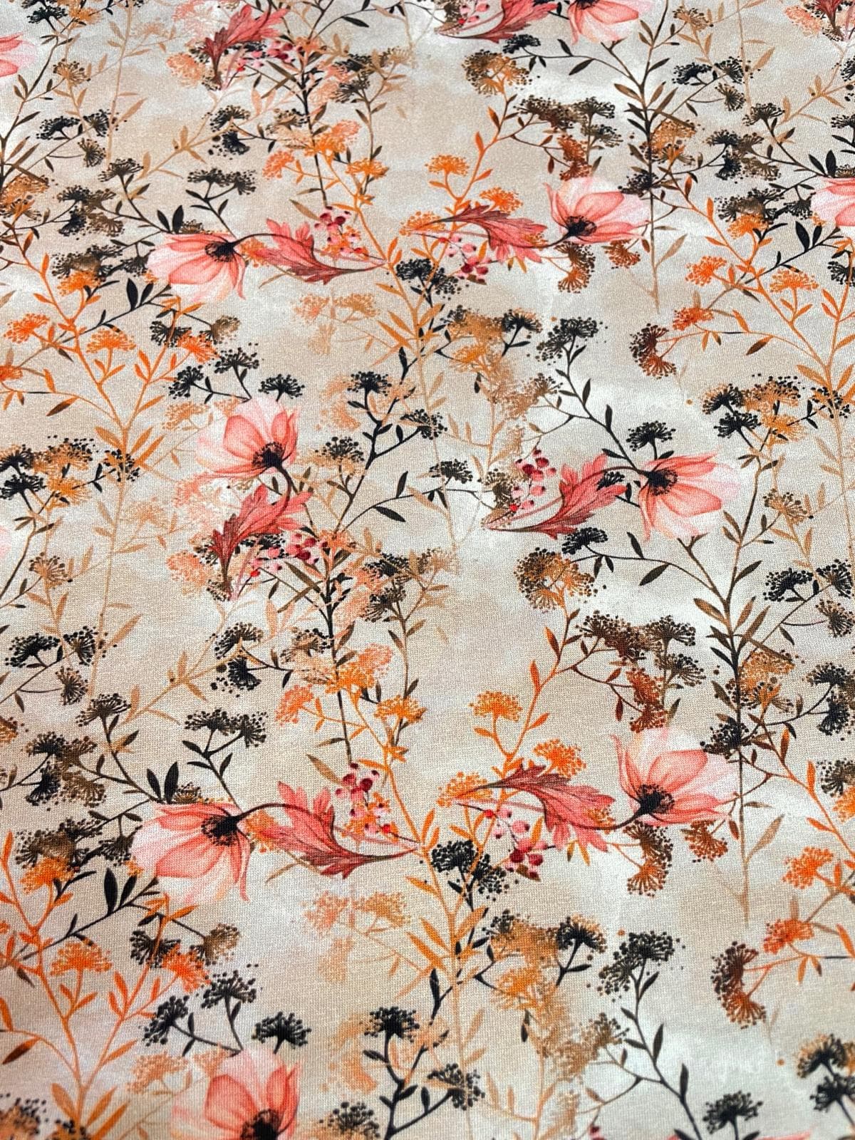 Elastischer Jerseystoff mit filigranem botanischem Print aus Gräsern und Blüten in Altrosa und Erdtönen auf einem naturfarbenen Hintergrund.