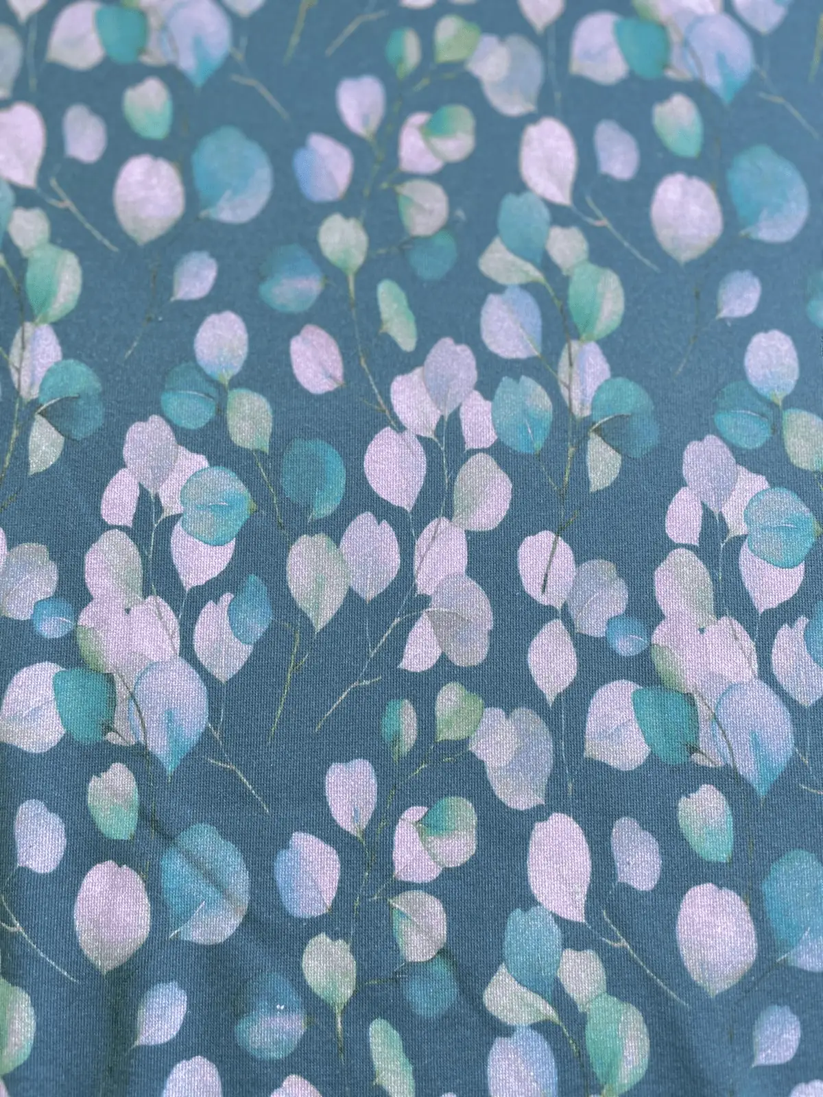 Sweatstoff als Meterware mit Eukalyptus-Aquarell-Muster in Petrol, Mint und Flieder (95% Baumwolle, 5% Polyester).