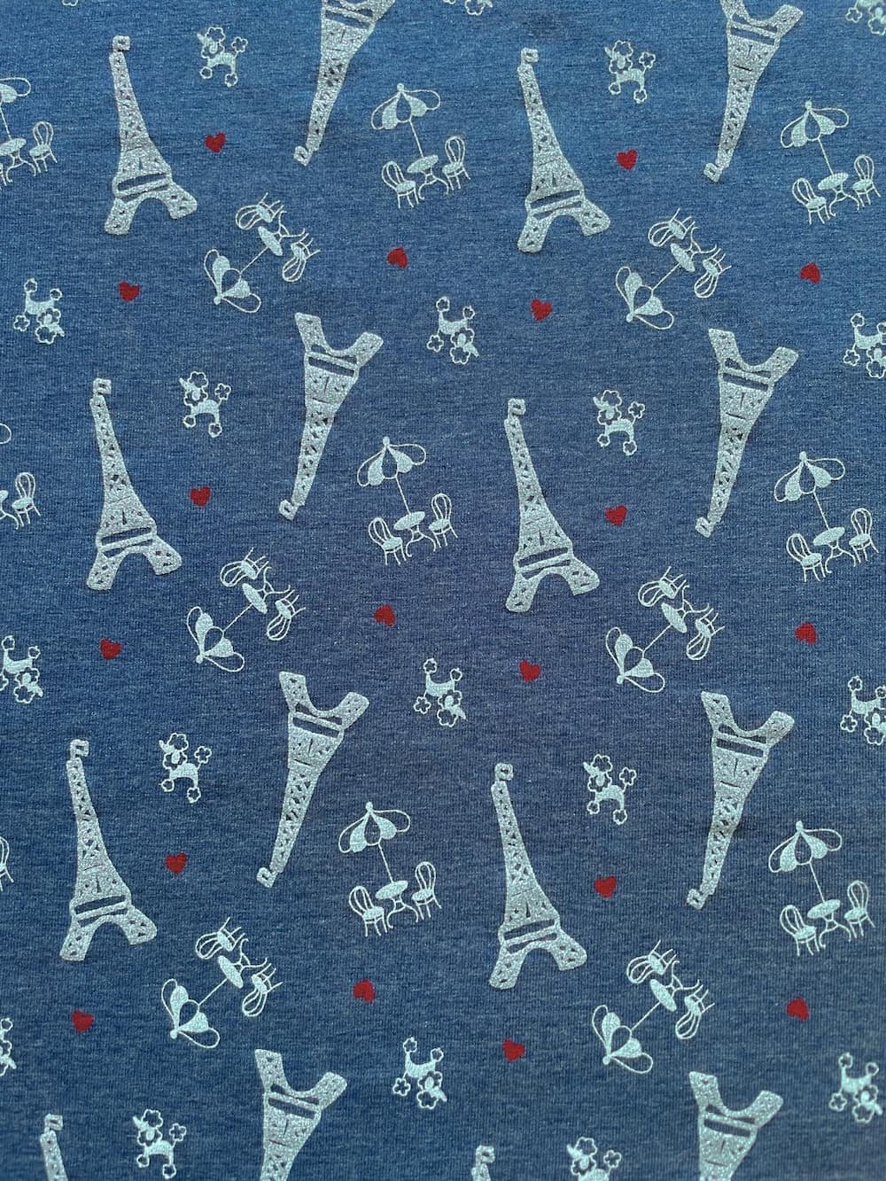Hochwertiger blauer Jersey-Stoff als Meterware, bedruckt mit silbernen Glitzer-Motiven vom Eiffelturm, kleinen Pudeln, Straßencafés und roten Herzen. Der verspielte Paris-Print auf elastischem Baumwolljersey ist ideal für glitzernde Kinderkleidung und Dam