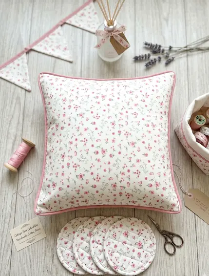 Feine Baumwolle Popeline mit zartem Streublumen-Muster in Rosa und Weiß, flachliegend präsentiert als Dekokissen, Wimpelkette und Untersetzer.