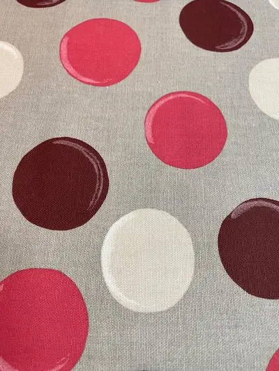 Nahaufnahme von beschichteter Baumwolle mit großen Punkten in Beerenrot, Weinrot und Creme auf grauem Hintergrund