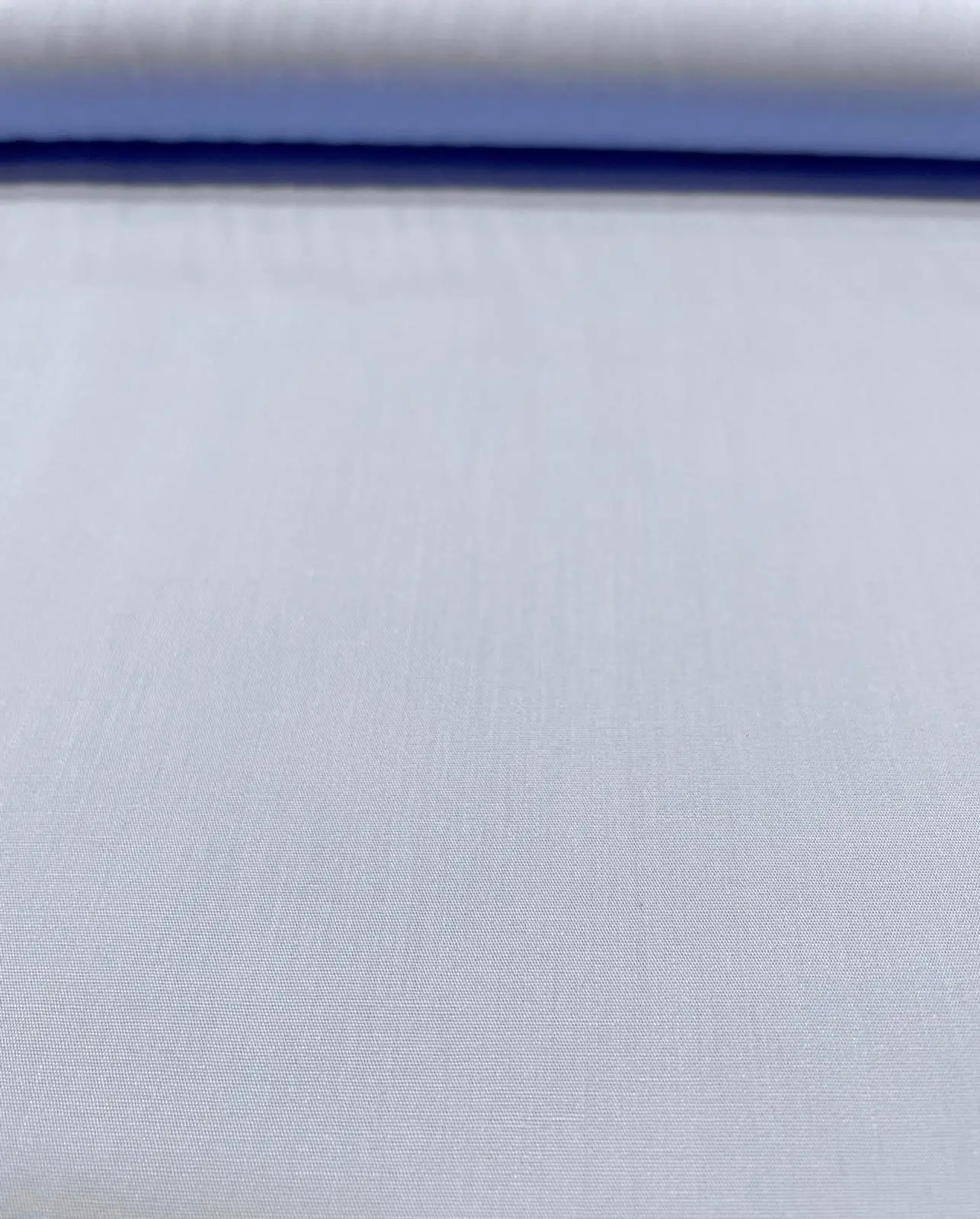 Glatt präsentierter, unelastischer Baumwollstoff als Meterware in einem feinen, hellen Blauviolett, der am oberen Bildrand sauber über eine Stoffrolle gewickelt ist und eine dichte, gleichmäßige Webstruktur zeigt.