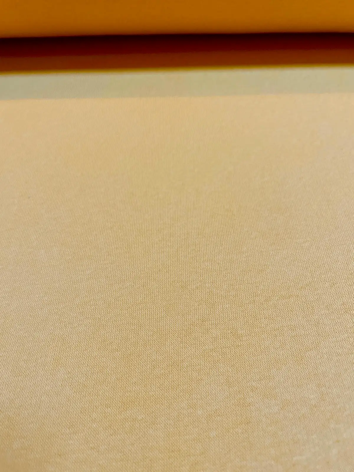 Nahaufnahme von Sweat Meterware in einem gedeckten Gelb mit feiner Oberflächenstruktur