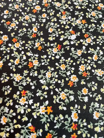 Beschichtete Baumwolle mit kleinen weißen und orangefarbenen Blüten, Millefleurs-Design auf dunklem Hintergrund, abwaschbare Meterware.