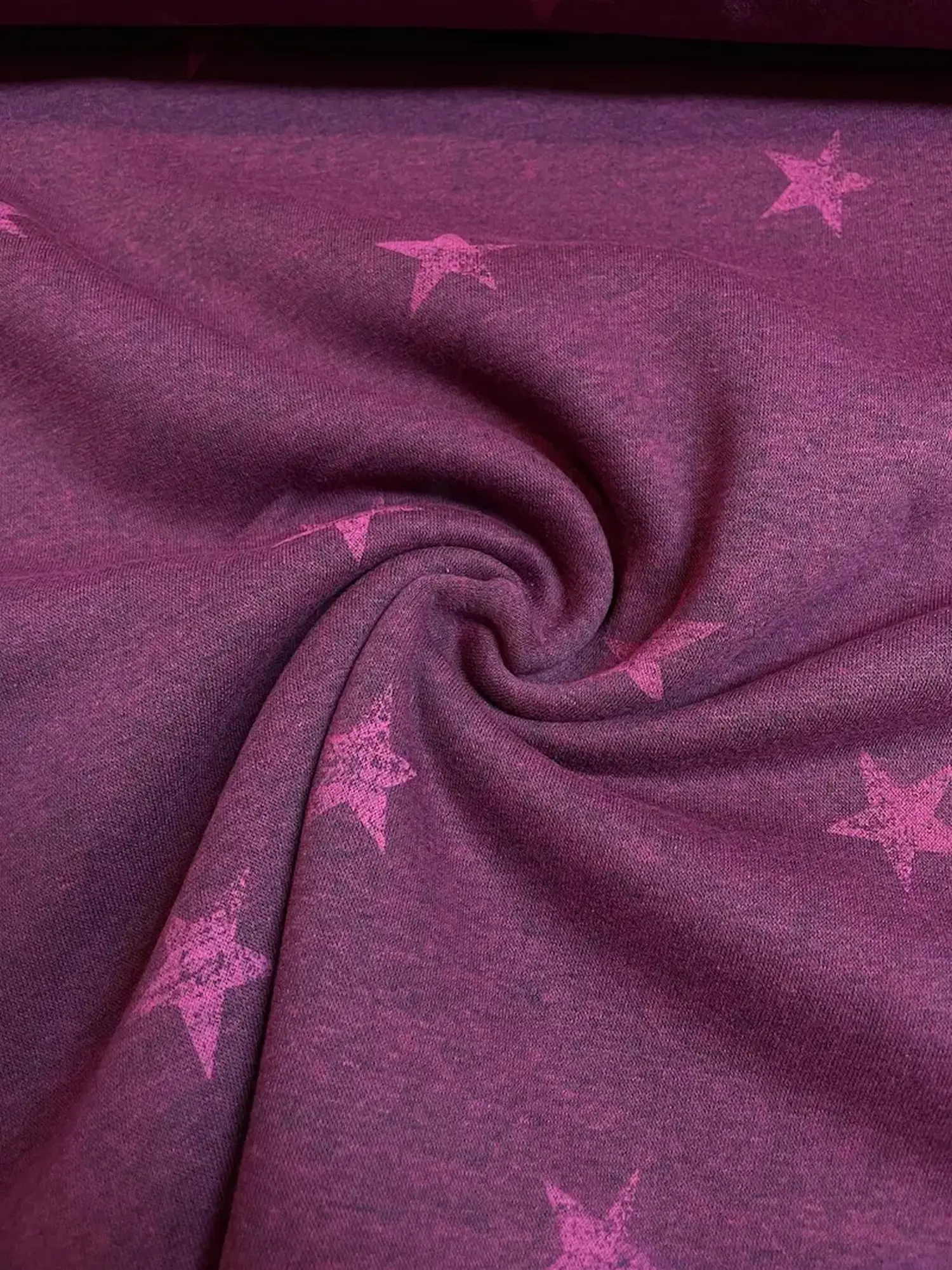 Angerauter Sweatstoff mit flauschiger Innenseite. Das florale Muster zeigt hellblaue Blüten auf einem kräftigen beerenfarbenen Hintergrund.