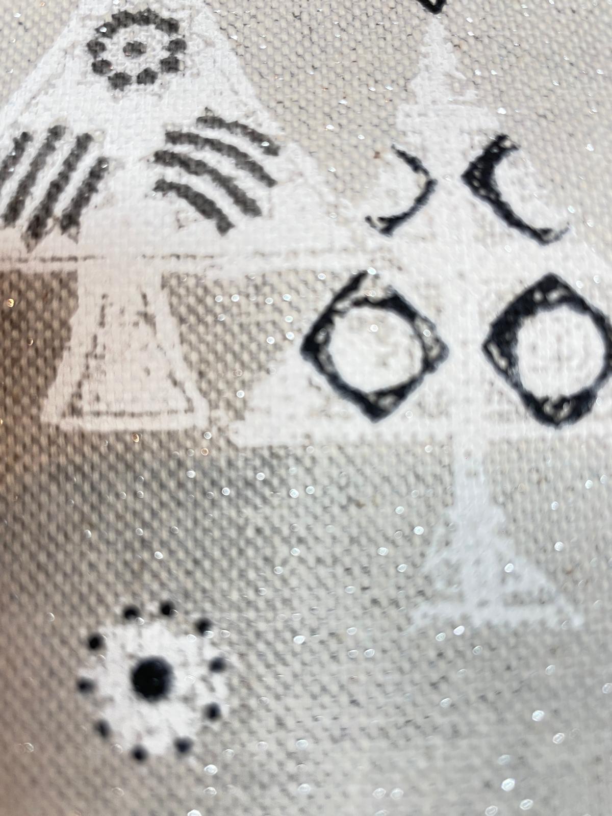 Nahaufnahme eines festlichen Deko- und Baumwollstoffs als Meterware mit starkem Glitzer-Effekt, skandinavischen Tannenbäumen und geometrischen Mustern in Schwarz und Weiß auf grauem Hintergrund.
