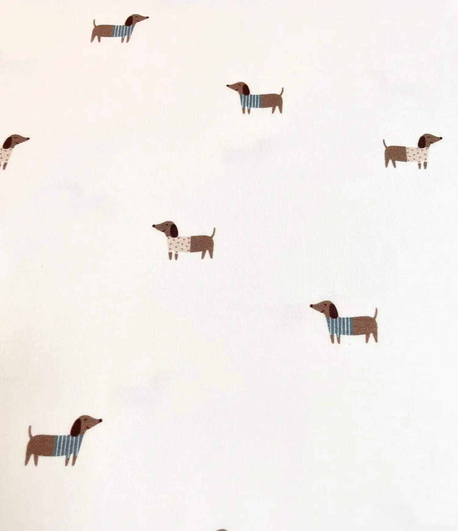 Heller Jersey-Stoff mit einem verspielten Streumuster aus kleinen braunen Dackeln auf weißem Hintergrund. Die Hunde tragen niedliche Pullover in Blau-Weiß gestreift oder mit Punkten. Ein idealer Stoff für Baby- und Kinderkleidung sowie für Hundeliebhaber.