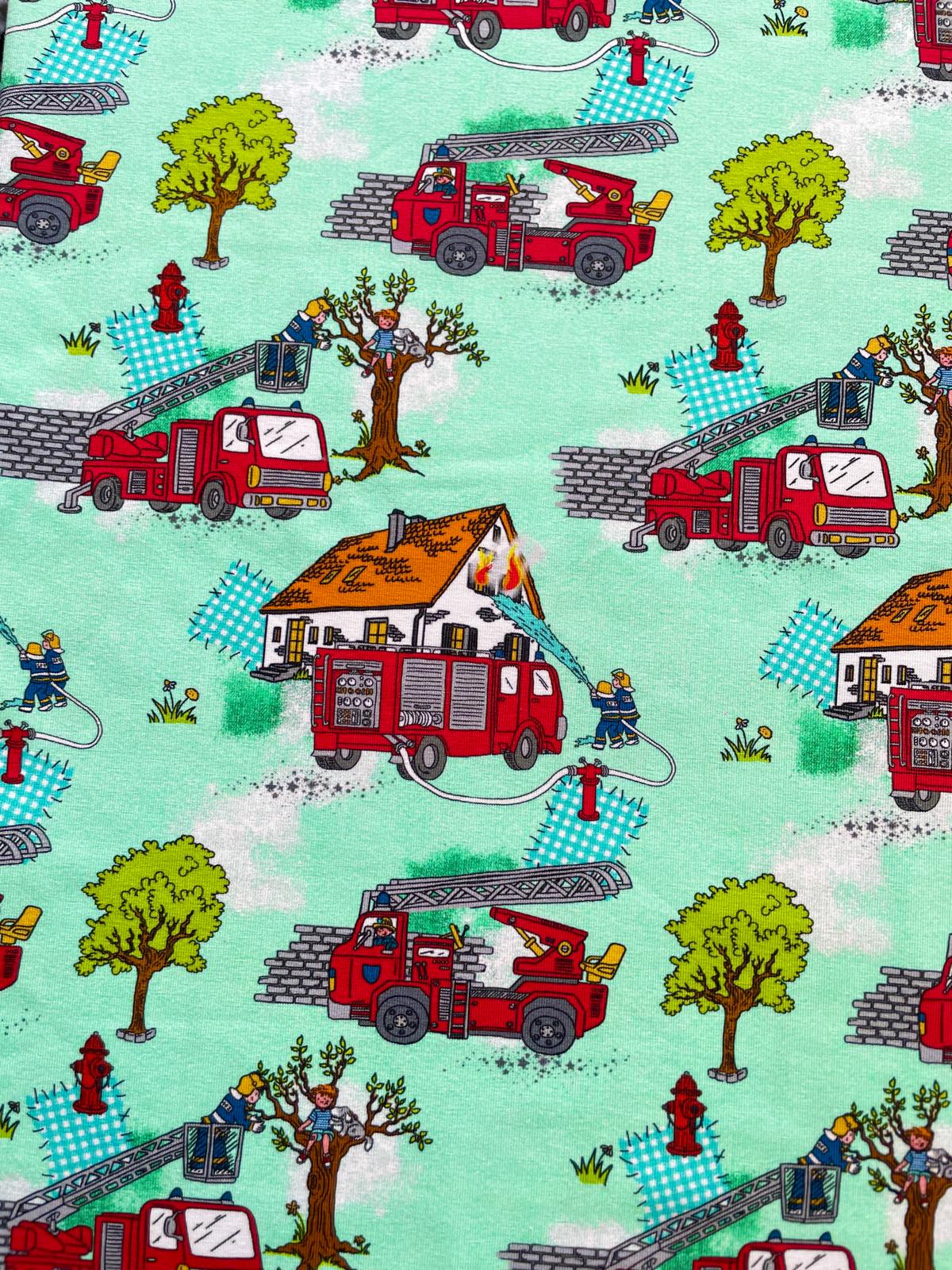 Detailaufnahme eines mintgrünen Jerseystoffs mit bunten Feuerwehrauto-Motiven, Löschszenen und Bäumen für Kinderbekleidung.