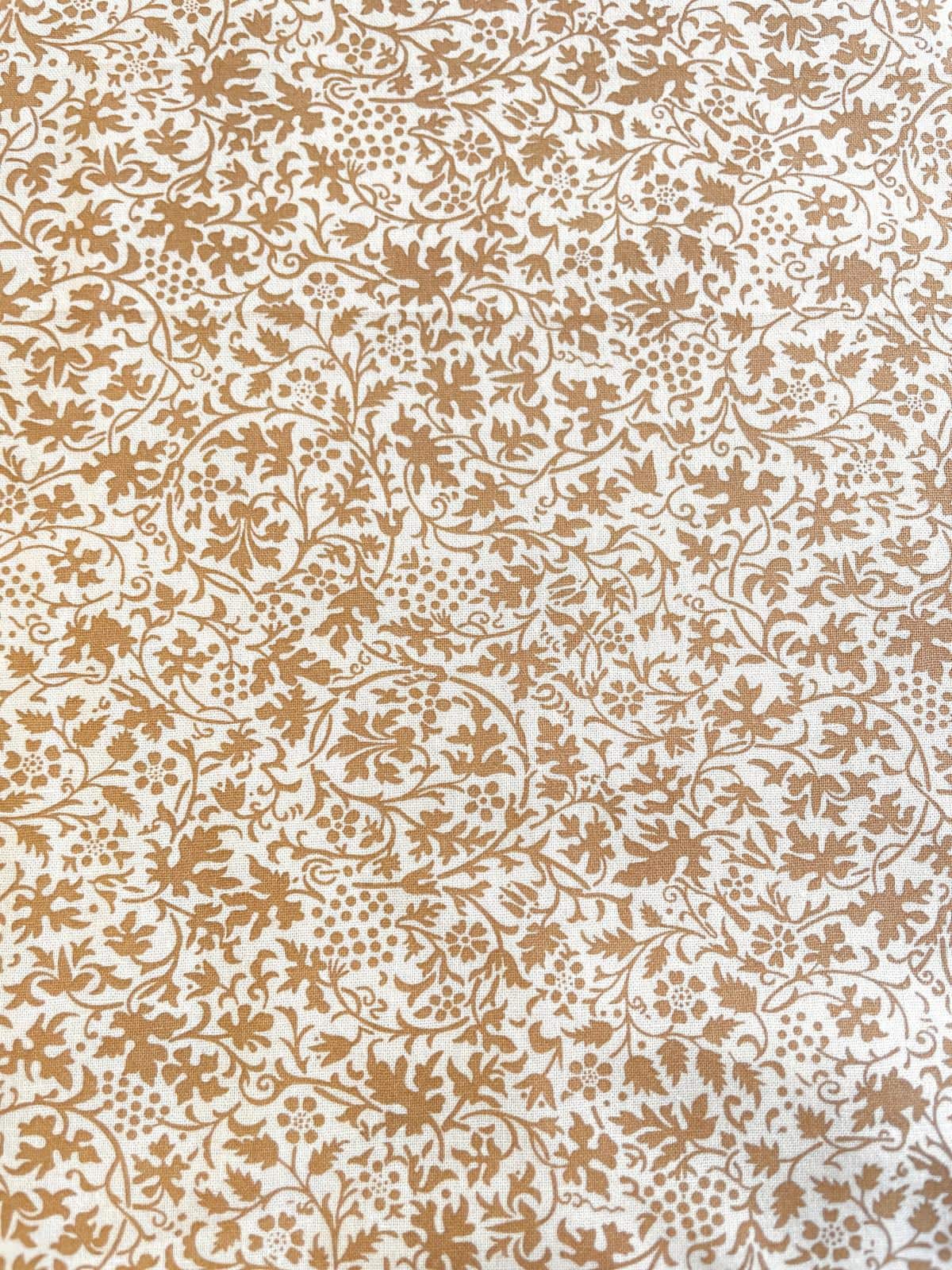 Nahaufnahme von weißer Baumwoll-Webware als Meterware mit einem filigranen, detailreichen Ornament- und Rankenmuster in Bronze