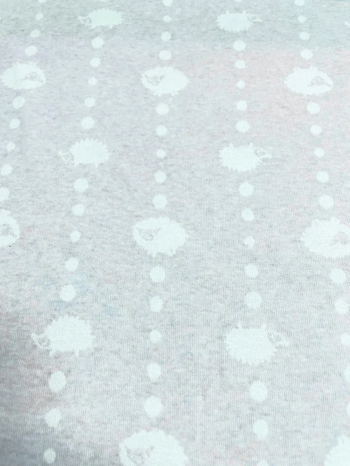 Hochwertiger Strick-Jacquard in hellem Graublau mit Melange-Effekt. Das eingestrickte Muster zeigt weiße Schafe und kleine Punkte, die in vertikalen Reihen angeordnet sind. Die weiche, strukturierte Oberfläche des blickdichten Stoffes ist ideal für Baby-