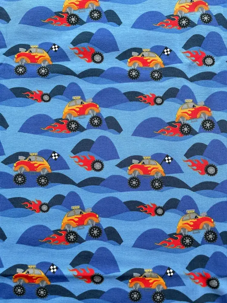 Blauer Baumwolljersey-Stoff mit Rapport-Muster aus roten und gelben Monster Trucks mit Flammen-Details auf dunkelblauen Hügeln.